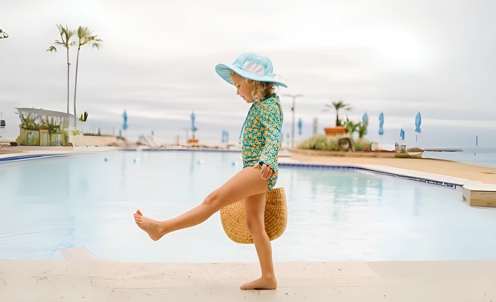 A girl in sun-protective swimwear with a wide-brimmed sun hat by the pool—10 ways to keep your kids safe during summer vacation