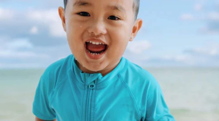 Boy in a Scuba Blue rash guard by SwimZip on the beach—Are blue swimsuits safe