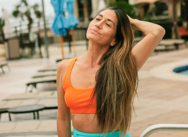 A woman by the pool wearing SwimZip's bright orange bikini top—Are orange swimsuits safe?