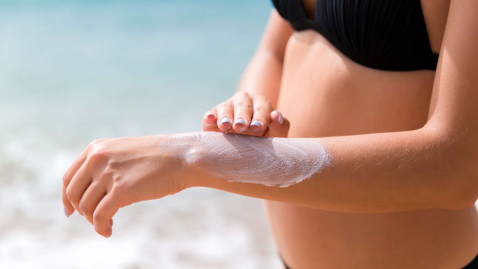 Woman on the beach puts sunscreen on her arm—How long does it take to tan in UV 7?