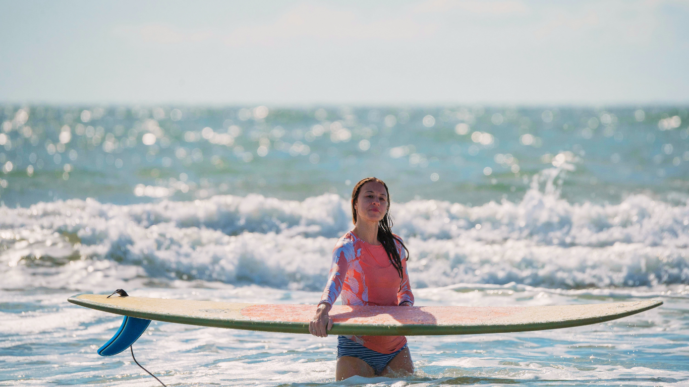 Woman with surfboard wearing peach rash guard—What are rash guards made of?