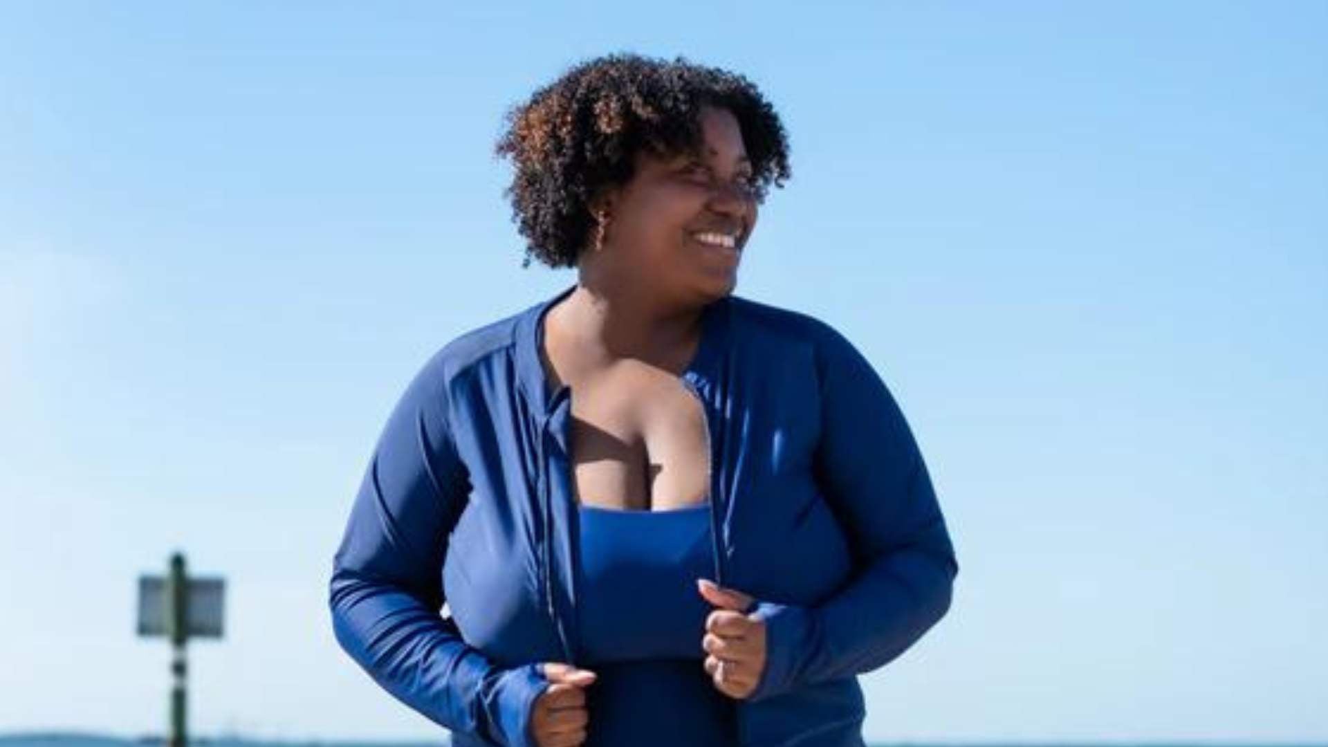 Woman in SwimZip's swim shorts, black halter top, and navy rash guard—What are the best swimsuits for larger busts?