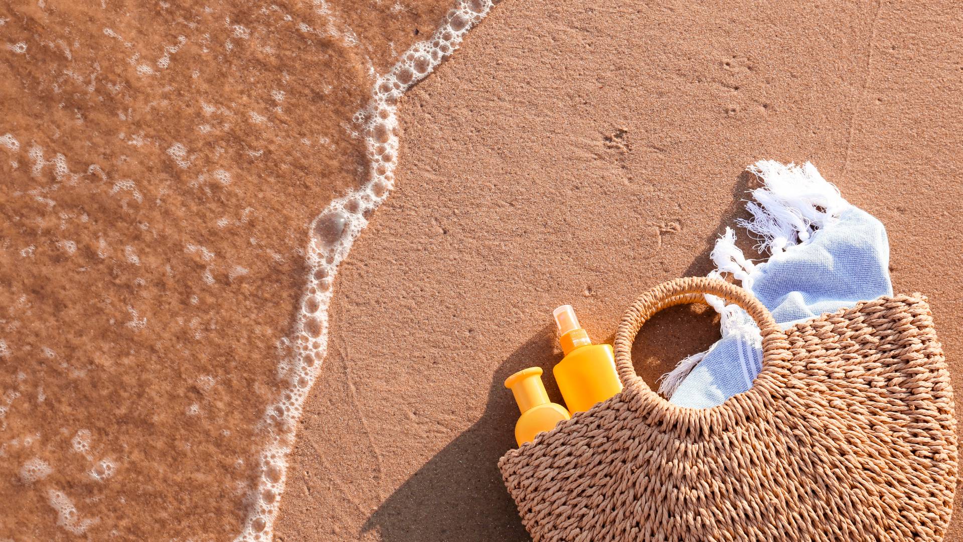 Beach bag with sun protection products and a blanket at the beach—What to pack in a girl's beach bag for a perfect beach day