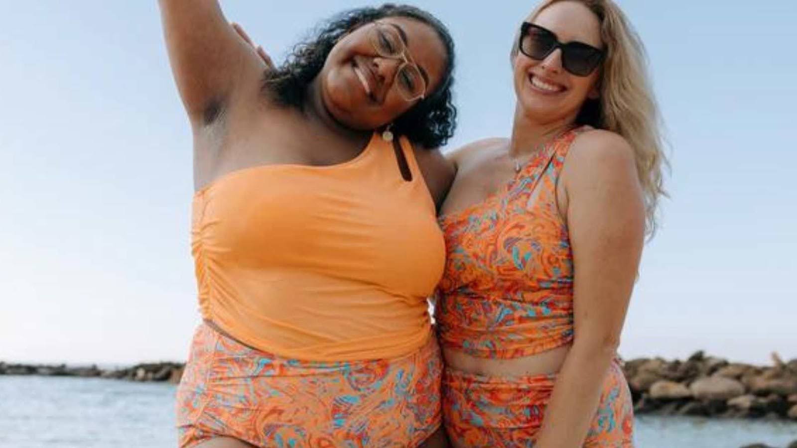 Two women in orange one-shoulder tops at the beach—Best slimming swimsuits
